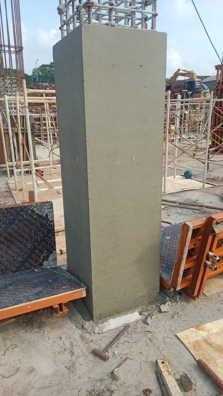 Kolom beton hasil pengecoran dengan permukaan rata, panel bekisting tersusun di sampingnya