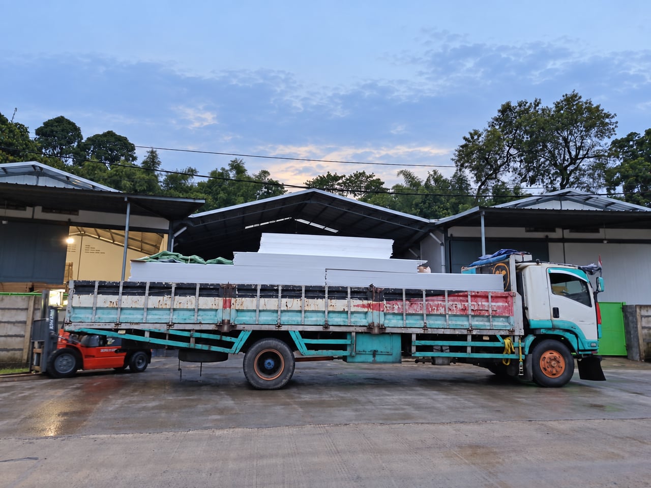 Foto disunting: muatan panel atap putih di atas truk di depan gudang